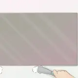 Aplicando adhesivo en la parte inferior de un espejo sin marco, un paso clave para saber como colgar un espejo sin marco.