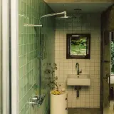 Baños pequeños con ducha, lavabo y espejo con vista a un jardín. Paredes de azulejos verdes y piedra natural.