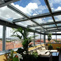 Disfruta de vistas panorámicas desde este cerramiento parcial terraza ático. Sofá cómodo, plantas y un cielo azul con nubes.