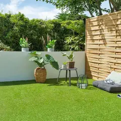 Terraza con césped artificial verde vibrante, plantas en macetas, un banco y una valla de madera.