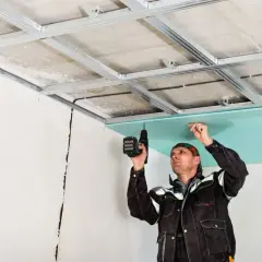 Un trabajador instala una placa de yeso verde en un techo metálico, un paso clave en como hacer una pared de pladur.