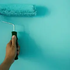Mano sujetando un rodillo de pintura turquesa, ideal para conseguir el mejor rodillo para pintar paredes lisas.
