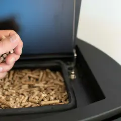 Mano añadiendo pellets a una estufa de pellets.