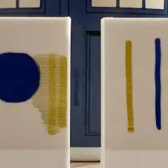 Dos lienzos blancos con trazos azules y amarillos. El fondo es una puerta azul, como si fuera una imprimación para un proyecto.