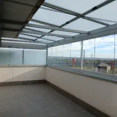 Terraza con cerramiento abatible de cristal, creando un espacio moderno y luminoso con vistas al exterior.
