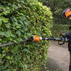 Hombre con equipo de protección realizando la poda de setos con una cortasetos eléctrica.