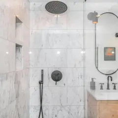 Ducha empotrada con grifo negro y rociador superior. La pared de mármol blanco tiene nichos empotrados.