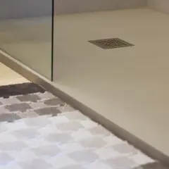 Plato de ducha blanco moderno con desagüe cuadrado. Alfombra a cuadros en primer plano.