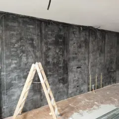 Instalación de material para insonorizar pared sin obra. Una escalera de madera apoya contra la pared cubierta con láminas negras.