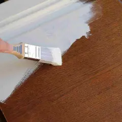 Pintando una puerta de madera ya pintada con brocha y pintura blanca.