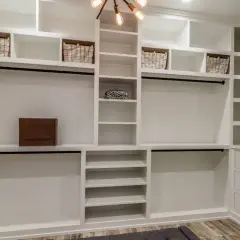 Amplio armario de pladur blanco con estantes, cestas, barras para colgar y cajones. Un bolso Louis Vuitton descansa en un estante.