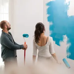 Pareja pintando una pared de azul. Él mira al techo, ella pinta. ¿Qué se pinta primero el techo o las paredes?