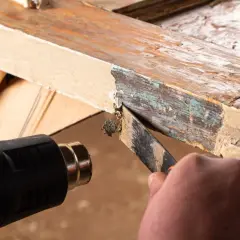 Cómo quitar la pintura de la madera sin lijar: se usa pistola de calor y rasqueta para despegar capas viejas de pintura de un marco de madera.