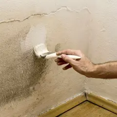 Pintando una pared con humedad. Se aplica pintura blanca con brocha sobre una zona manchada, buscando la mejor que pintura usar para paredes con humedad.