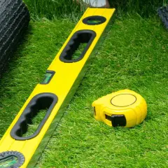 Manos enguantadas preparan el césped artificial. Nivel y cinta métrica listos para pegar.