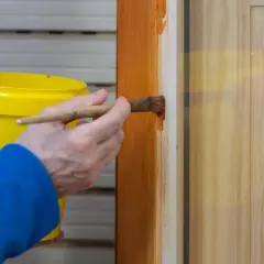 Persona aplica barniz a puertas de madera con brocha.