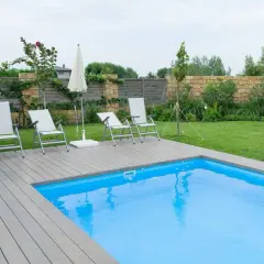 Sillas y sombrilla junto a la piscina, con un suelo de madera que rodea el agua azul.