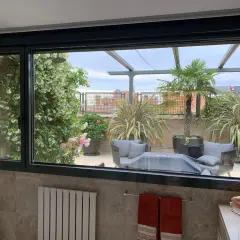 Ventana con perfil de aluminio negro, vista a terraza con plantas y mobiliario. ¿Cual es el mejor perfil de aluminio para ventanas?