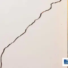 Grieta profunda en pared blanca, junto a marco amarillo y puerta de madera. Aprende como arreglar grietas profundas en paredes.