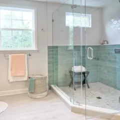 Instalar mampara ducha frontal corredera: baño moderno con ducha de cristal, azulejos verdes y ventana.