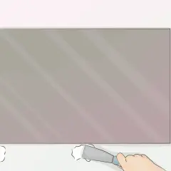 Aplicando adhesivo en la parte inferior de un espejo sin marco, un paso clave para saber como colgar un espejo sin marco.