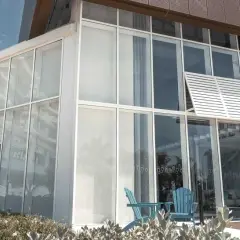 Edificio moderno con un **muro cortina fachada** de cristal. Dos sillas azules esperan en la entrada, reflejando palmeras.