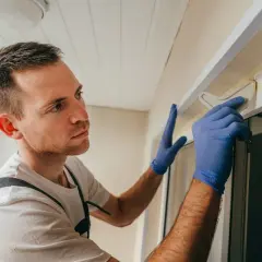 Hombre con guantes azules usa herramienta para quitar silicona de mampara.