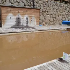 Una piscina de sal con agua turbia y una pared de duchas de madera.