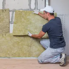 Obrero instala material aislante para aislar paredes del frío. La lana mineral se coloca entre perfiles metálicos.