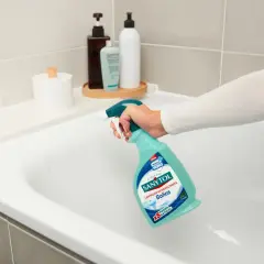 Mano rociando limpiador Sanytol en bañera blanca para quitar manchas oscuras plato ducha.
