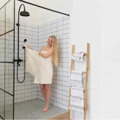 Mujer rubia envuelta en toalla junto a mampara de ducha moderna. Explora los tipos de mamparas de ducha para tu baño.
