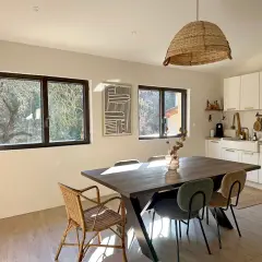 La cara de un cristal refleja la luz del sol en un comedor rústico con mesa de madera y sillas de mimbre.