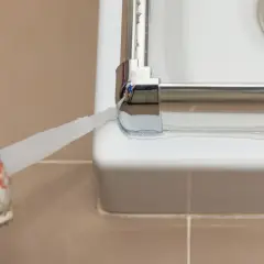 Aplicando sellador para mampara de ducha. Un aplicador de silicona deposita un cordón blanco para sellar la unión entre la mampara y la bañera.