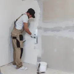Un obrero aplica yeso a una pared con una llana. Aprende como hacer yeso para renovar tu hogar.