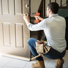 Hombre con taladro y cinturón de herramientas, aprendiendo como desmontar una cerradura de puerta interior.