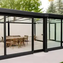 Modernos cerramientos de ventanas de cristal con estructura negra, creando un comedor exterior con mesa y sillas.