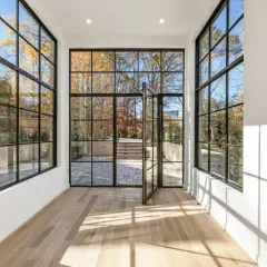 Amplio salón con grandes ventanales de aluminio y madera que dan a un jardín otoñal.