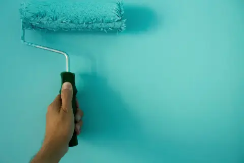 Mano sujetando un rodillo de pintura turquesa, ideal para conseguir el mejor rodillo para pintar paredes lisas.
