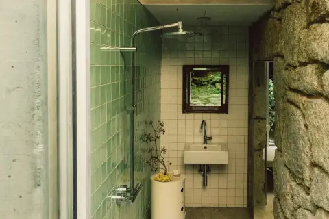 Baños pequeños con ducha, lavabo y espejo con vista a un jardín. Paredes de azulejos verdes y piedra natural.