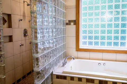 Duchas con paves de vidrio separan la bañera de la zona de ducha. La luz se filtra a través de la ventana de paves.