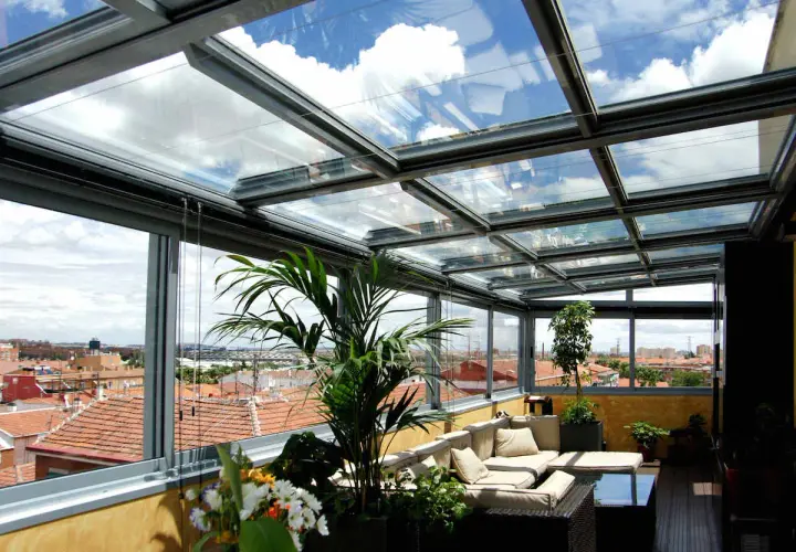 Disfruta de vistas panorámicas desde este cerramiento parcial terraza ático. Sofá cómodo, plantas y un cielo azul con nubes.