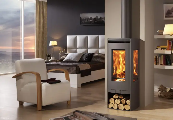 Estufa de leña moderna con fuego encendido, junto a una cama y sillón. Diversos tipos de estufas de gas ofrecen alternativas eficientes.