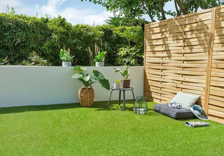 Terraza con césped artificial verde vibrante, plantas en macetas, un banco y una valla de madera.