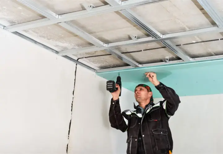 Un trabajador instala una placa de yeso verde en un techo metálico, un paso clave en como hacer una pared de pladur.