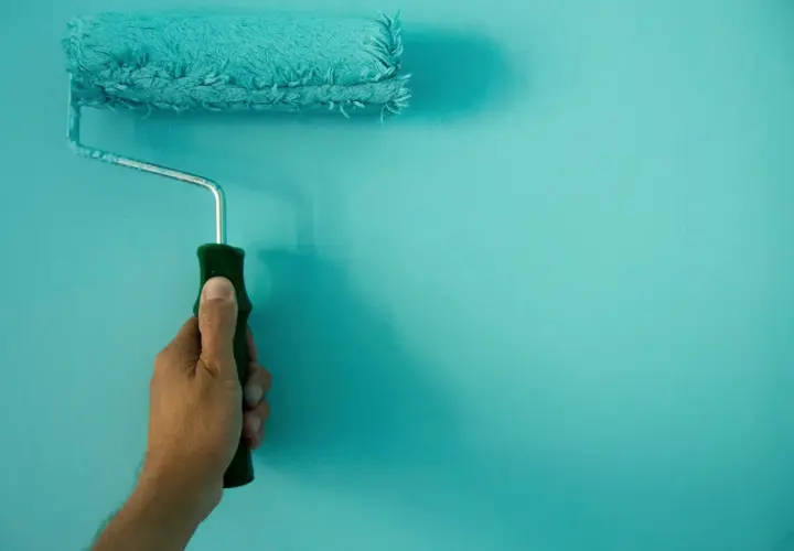 Mano sujetando un rodillo de pintura turquesa, ideal para conseguir el mejor rodillo para pintar paredes lisas.