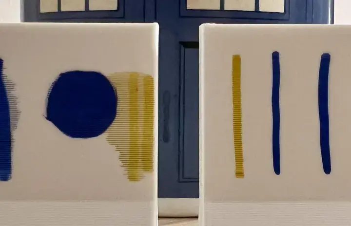 Dos lienzos blancos con trazos azules y amarillos. El fondo es una puerta azul, como si fuera una imprimación para un proyecto.