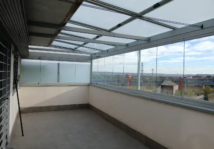 Terraza con cerramiento abatible de cristal, creando un espacio moderno y luminoso con vistas al exterior.