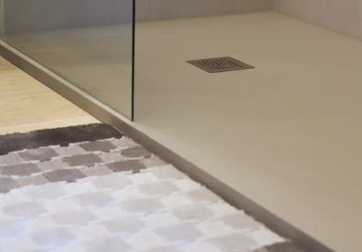 Plato de ducha blanco moderno con desagüe cuadrado. Alfombra a cuadros en primer plano.