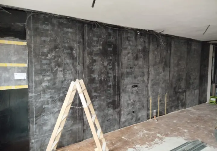 Instalación de material para insonorizar pared sin obra. Una escalera de madera apoya contra la pared cubierta con láminas negras.