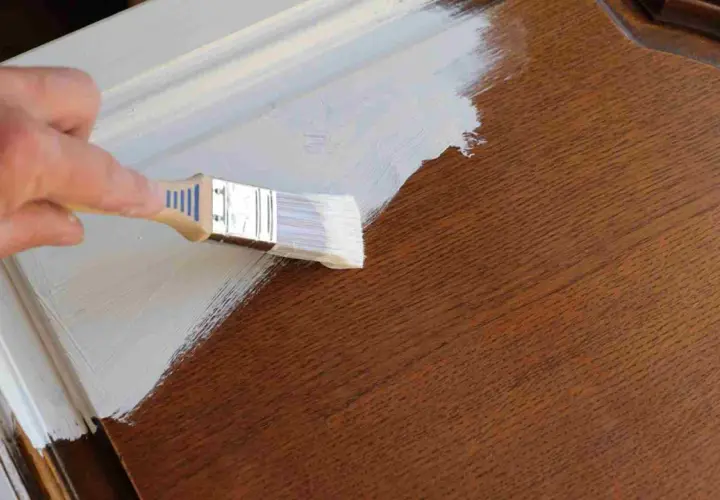 Pintando una puerta de madera ya pintada con brocha y pintura blanca.